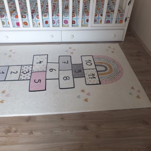 May include: A white rug with a hopscotch design featuring numbers 1 through 11. The rug also has a rainbow and pink hearts.