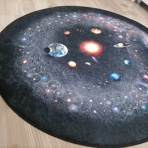 Puede incluir: Una alfombra ovalada con un dise&ntilde;o detallado del sistema solar. El dise&ntilde;o muestra planetas, estrellas y galaxias sobre un fondo oscuro. Los planetas son de varios colores y la alfombra tiene bordes oscuros.