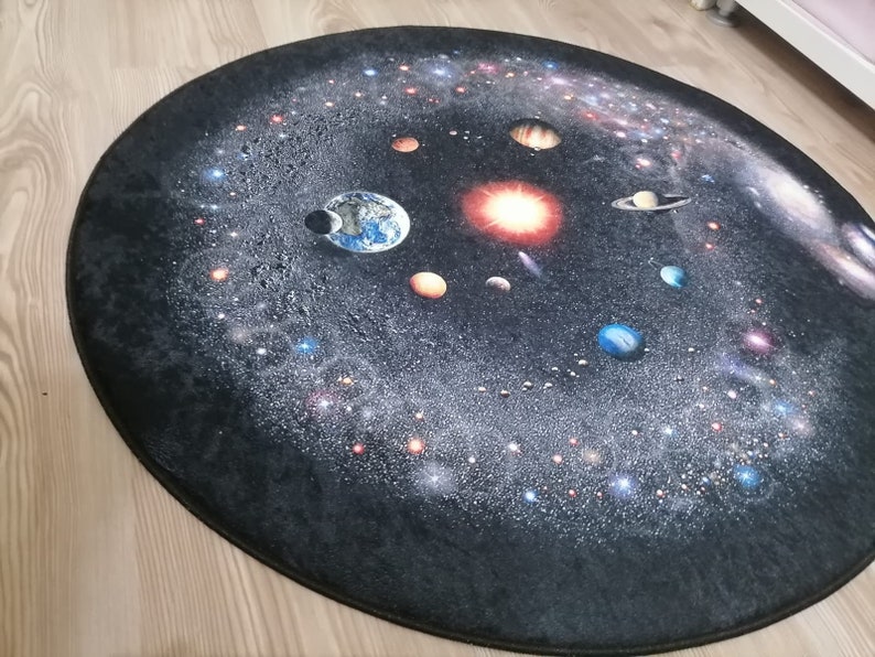 Puede incluir: Una alfombra ovalada con un dise&ntilde;o detallado del sistema solar. El dise&ntilde;o muestra planetas, estrellas y galaxias sobre un fondo oscuro. Los planetas son de varios colores y la alfombra tiene bordes oscuros.