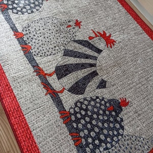 May include: A grey runner rug featuring a repeating pattern of stylised chickens perched on a dark blue branch. The chickens have black and white patterned bodies and red accents. The rug has a red border.