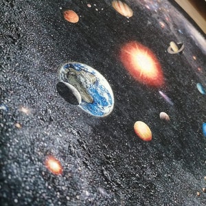 Puede incluir: Una alfombra redonda con una representaci&oacute;n detallada del sistema solar. La alfombra muestra planetas, estrellas y galaxias sobre un fondo oscuro, similar al espacio. La Tierra es visible con sus oc&eacute;anos azules y nubes blancas. J&uacute;piter, Saturno y Marte tambi&eacute;n son visibles.
