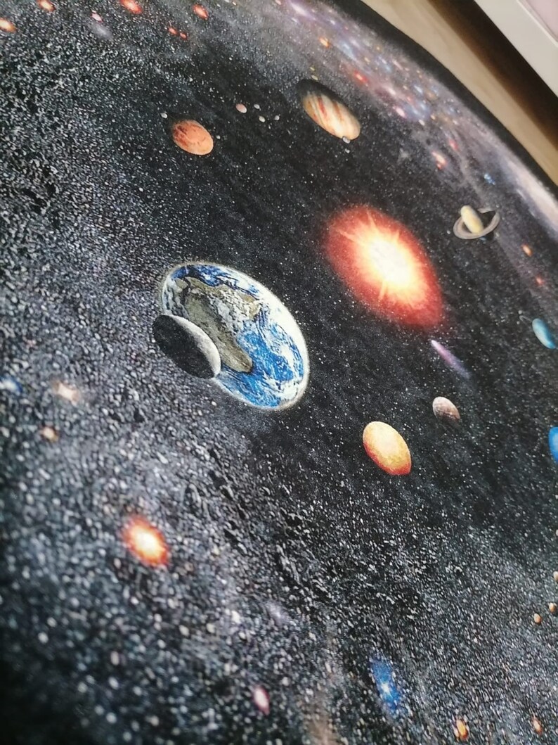 Puede incluir: Una alfombra redonda con una representaci&oacute;n detallada del sistema solar. La alfombra muestra planetas, estrellas y galaxias sobre un fondo oscuro, similar al espacio. La Tierra es visible con sus oc&eacute;anos azules y nubes blancas. J&uacute;piter, Saturno y Marte tambi&eacute;n son visibles.