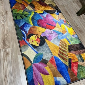 May include: Abstract rug with a colorful design featuring geometric shapes, flowers, and a woman's face. The rug has a dark gray border.