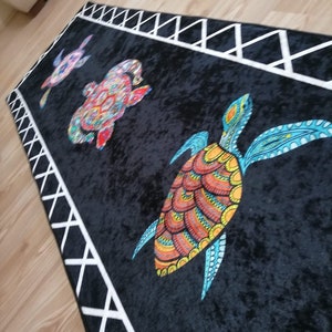 May include: Black rectangular rug featuring three colorful sea turtles. The turtles have intricate patterns in shades of red, orange, yellow, and blue. The rug has a white geometric border.