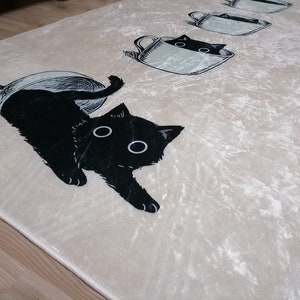 May include: A white rug with a black cat design. The cat is peeking out of a teacup. The rug has a soft, velvety texture.