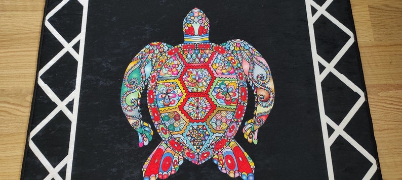 May include: A black rectangular rug featuring a colorful turtle design. The turtle is intricately patterned with red, yellow, blue, and green geometric shapes and floral motifs. White geometric border accents the edges.