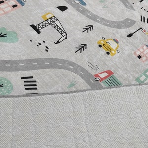 May include: A gray and white play mat with a city theme. The mat features a winding road, buildings, trees, cars, and a construction crane.