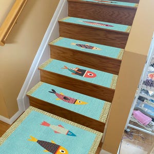Op de afbeelding: Een set van zes blauwe en beige antislip traptreden met een kleurrijk visontwerp. De treden zijn gemaakt van een zacht, getextureerd materiaal en hebben een antislip rug.