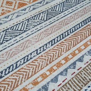 May include: A white rug with a geometric pattern in shades of orange, blue, and brown. The pattern is made up of stripes and zigzags.