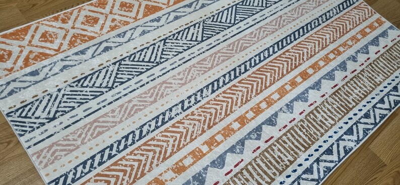 May include: A white rug with a geometric pattern in shades of orange, blue, and brown. The pattern is made up of stripes and zigzags.