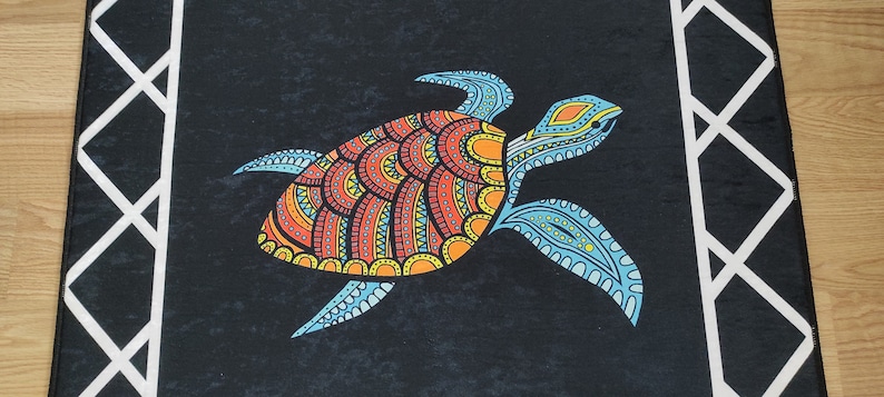 May include: A black rectangular rug featuring a colorful turtle design. The turtle has a patterned shell in orange, red, and yellow, with blue flippers and head. White geometric border on the sides.