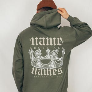 May include: Green hooded sweatshirt with a white graphic print of a crown and the text "name above all names Philippians 2:9"