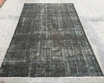 May include: Rectangular, distressed black rug with white and teal accents. The rug has a faded, vintage appearance, with a visible pattern and a white border. Suitable for living rooms or bedrooms.