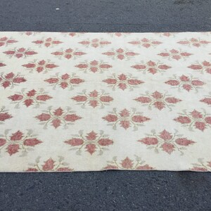 May include: A cream-colored rug with a repeating pattern of red floral designs. The rug has a subtle sheen and a soft texture.