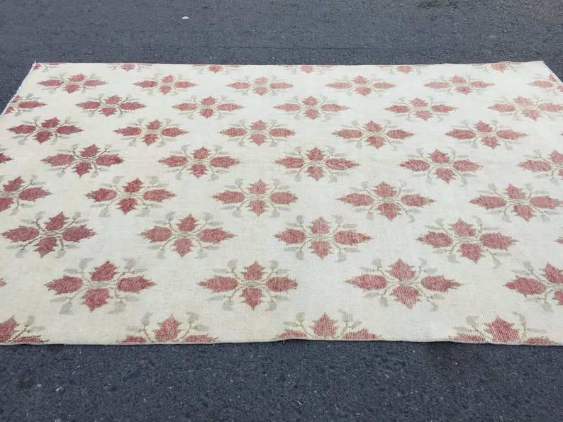 May include: A cream-colored rug with a repeating pattern of red floral designs. The rug has a subtle sheen and a soft texture.