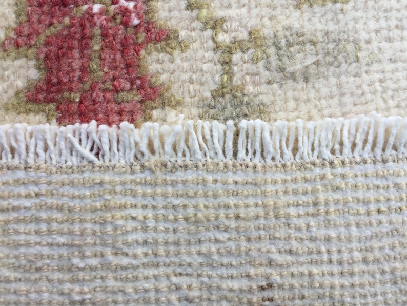 May include: Close-up of a white and beige woven rug with a fringe border. The rug has a subtle pattern of small squares.