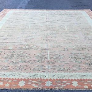 Könnte beinhalten: Ein Vintage-Teppich mit hellrosa und cremefarbenem Hintergrund und einem schwarzen Blumenmuster. Der Teppich hat einen pfirsichfarbenen Rand mit einem geometrischen Muster.