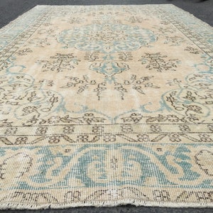 May include: A vintage rug with a light beige background and a blue and brown floral pattern. The rug has a fringed edge.