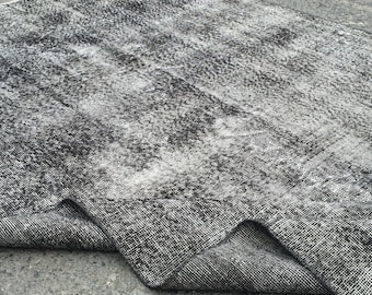 Pode incluir: Um tapete preto e branco desgastado com textura tecida. O tapete está dobrado ao meio e tem uma aparência desbotada.