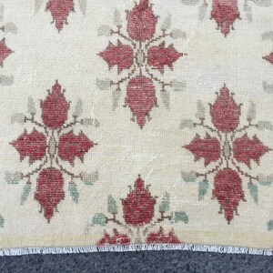 May include: A cream-colored rug with a repeating pattern of red floral motifs. The rug has a white fringe border.