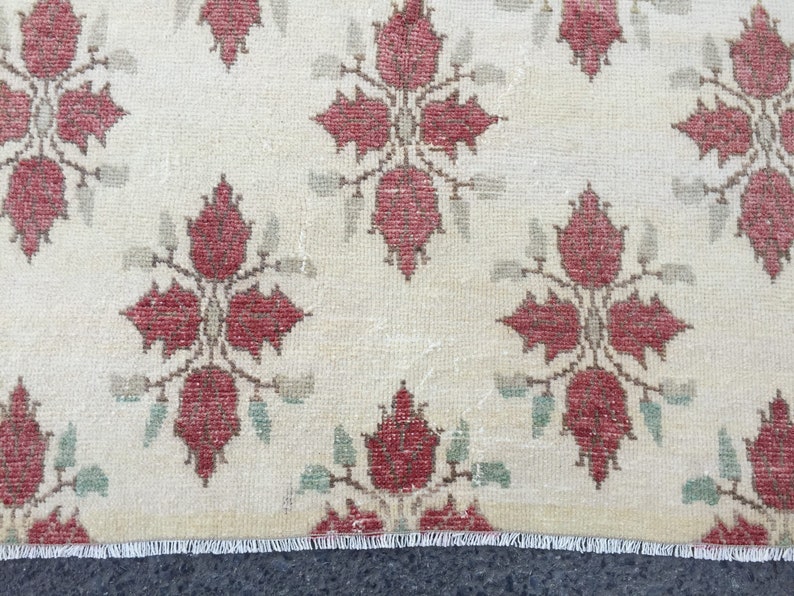 May include: A cream-colored rug with a repeating pattern of red floral motifs. The rug has a white fringe border.