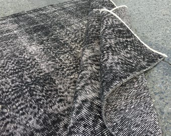 Pode incluir: Tapete com padrão preto e branco com um visual desgastado. O tapete está dobrado ao meio, mostrando a textura e o detalhe do padrão.