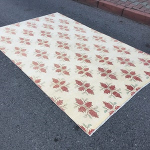May include: A cream-colored rug with a repeating pattern of red and green floral motifs. The rug has a fringed edge.