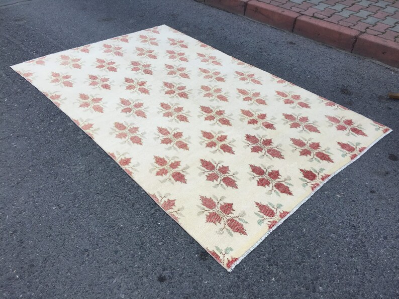 May include: A cream-colored rug with a repeating pattern of red and green floral motifs. The rug has a fringed edge.
