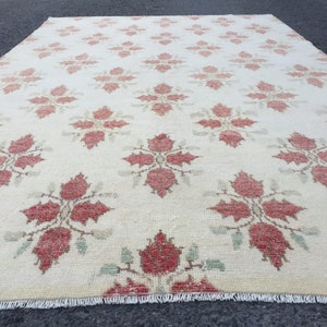 May include: A cream-colored rug with a repeating pattern of red floral designs. The rug has a fringe border.