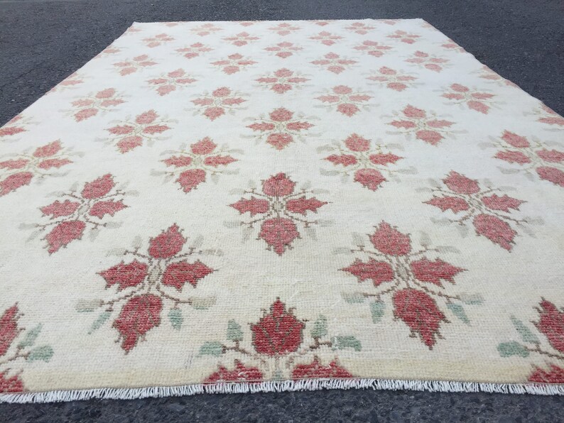 May include: A cream-colored rug with a repeating pattern of red floral designs. The rug has a fringe border.