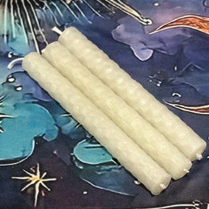 May include: Three off-white, cylindrical candles featuring a textured, honeycomb-like surface pattern. Each candle has a visible white wick at the top end. The candles are arranged side-by-side in a parallel formation, showcasing their uniform shape.