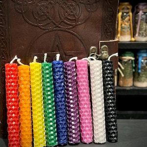 May include: A set of nine cylindrical candles arranged in a row, each featuring a textured honeycomb pattern. The candles are colored in red, orange, yellow, green, blue, purple, pink, white, and black, and each includes a white cotton wick.