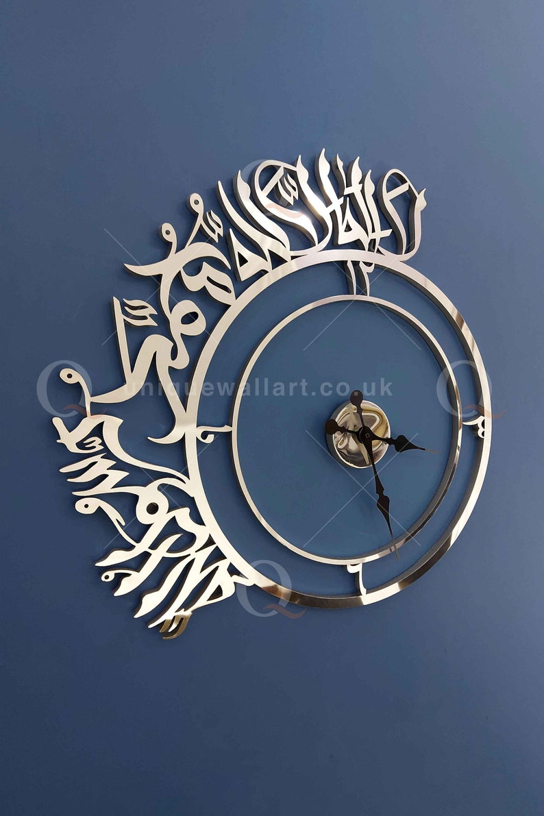 May include: A silver wall clock with Arabic calligraphy around the outer edge. The clock face is blue with silver hands and a silver center.
