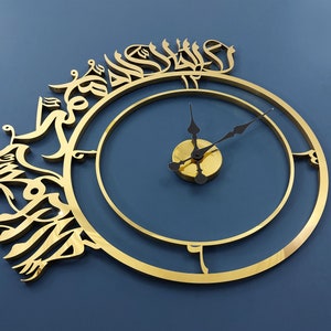 May include: A gold-colored clock with Arabic calligraphy around the outer edge. The clock face is a simple circle with black hands.