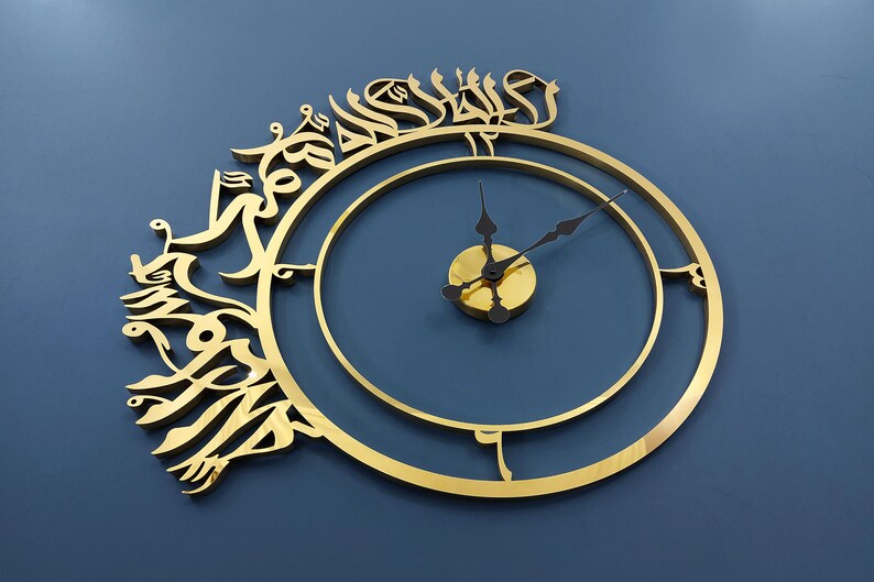 May include: A gold-colored clock with Arabic calligraphy around the outer edge. The clock face is a simple circle with black hands.