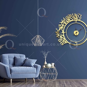 May include: A gold-colored wall clock with Arabic calligraphy around the clock face. The clock is hanging on a dark blue wall in a living room setting with a blue sofa, a plant, and a side table.