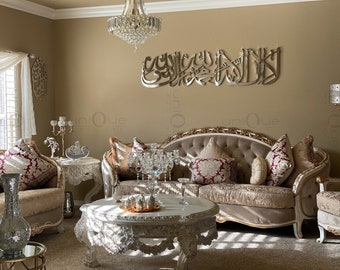May include: A living room interior with a beige sofa with gold trim and red and white patterned pillows. A white coffee table with ornate carvings sits in front of the sofa. A crystal chandelier hangs from the ceiling. A silver wall decor with Arabic calligraphy is on the wall behind the sofa.