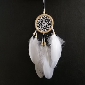 May include: A small, white and brown dreamcatcher with white feathers hanging from it. The dreamcatcher is hanging from a piece of driftwood.