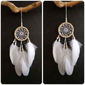 May include: A small, white and beige dreamcatcher with white feathers hanging from it. The dreamcatcher is hanging from a piece of driftwood.