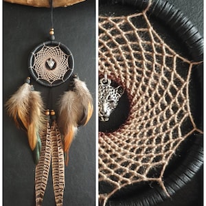 May include: A handmade dreamcatcher with a black hoop and a woven web design. The dreamcatcher features brown and orange feathers, wooden beads, and a silver charm. It is suspended from a wooden branch.