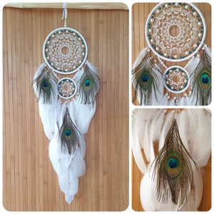May include: White dream catcher with peacock feathers. The dream catcher has three hoops with white beads and a white macrame design. The feathers are white with blue and green accents.