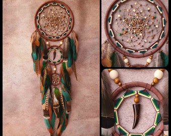 Puede incluir: Un atrapasueños marrón con plumas verdes y marrones, cuentas y un amuleto de diente de madera. El atrapasueños tiene un diseño circular con un patrón de telaraña y está decorado con cuentas y plumas.