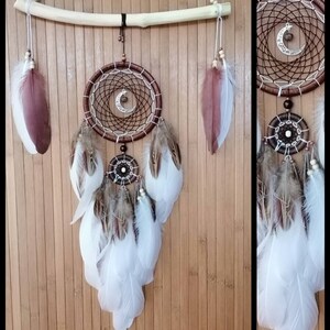 May include: A brown and white dreamcatcher with feathers hanging from the bottom. The dreamcatcher has a wooden hoop and a crescent moon charm. The feathers are white and brown.