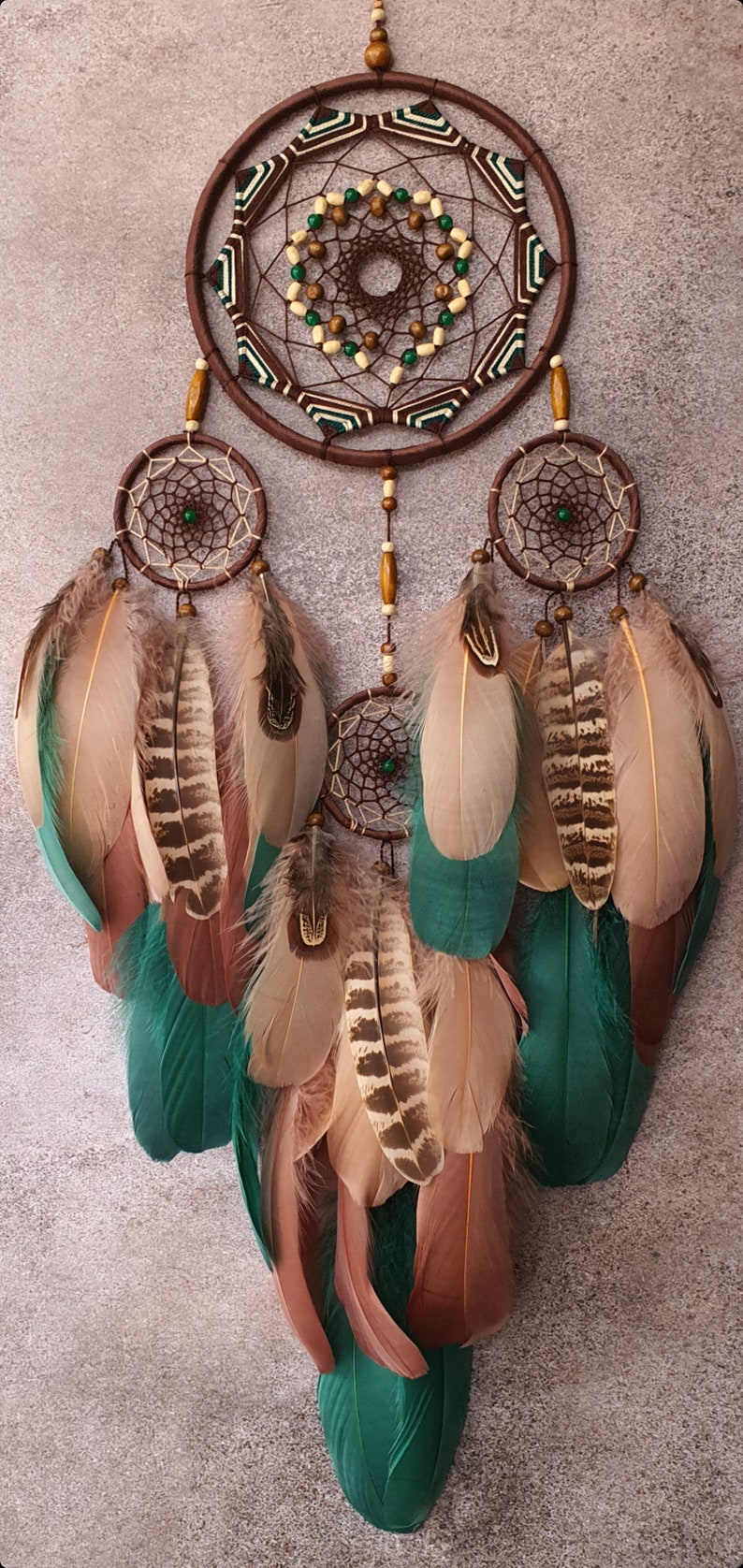May include: A brown dreamcatcher with green and white accents and feathers. The dreamcatcher has three smaller circles with beads and feathers hanging from them.