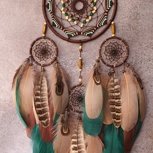 May include: A brown dreamcatcher with green and white accents and feathers. The dreamcatcher has a large central circle with a smaller circle inside. The feathers are brown, beige, and teal.