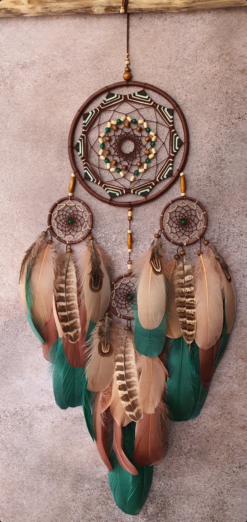 May include: A brown dreamcatcher with green and white accents and feathers. The dreamcatcher has a large central circle with a smaller circle inside. The feathers are brown, beige, and teal.
