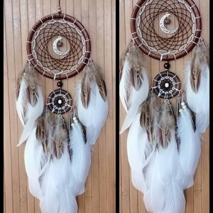 May include: A brown dream catcher with white feathers and a crescent moon charm. The dream catcher is hanging from a wooden surface.