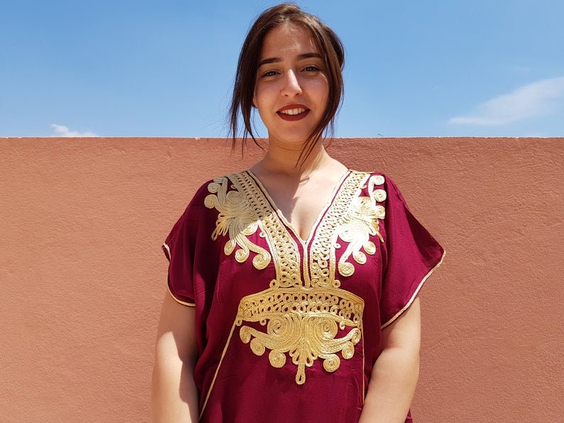 Op de afbeelding: Een vrouw draagt een bordeauxrode kaftan met gouden borduurwerk. De kaftan heeft een V-hals en korte mouwen.