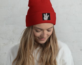 May include: Red beanie with a black patch featuring a white hand making a peace sign.