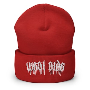 May include: A red beanie with the white text "WEST SIDE" embroidered on the front. The beanie is a solid color and has a folded brim. The text is in a gothic font.